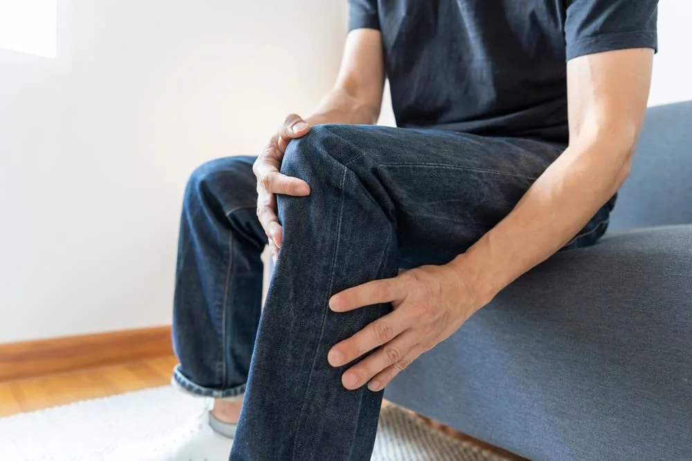 Close-up of a man's knee experiencing severe joint pain while sitting on a sofa.