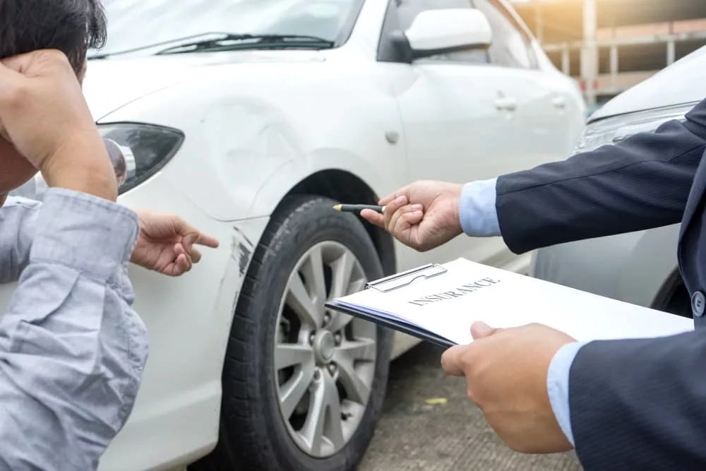 An insurance agent inspects crashed car with driver while doing the paperwork on the roadside of Miami, FL