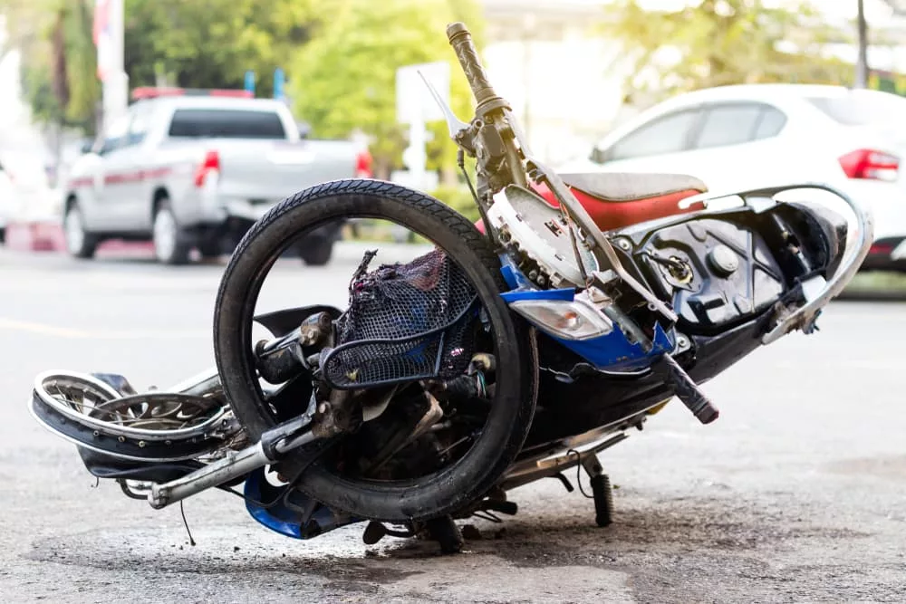 A severely damaged motorcycle after a serious accident, positioned on a paved road near a fence in Miami, FL.