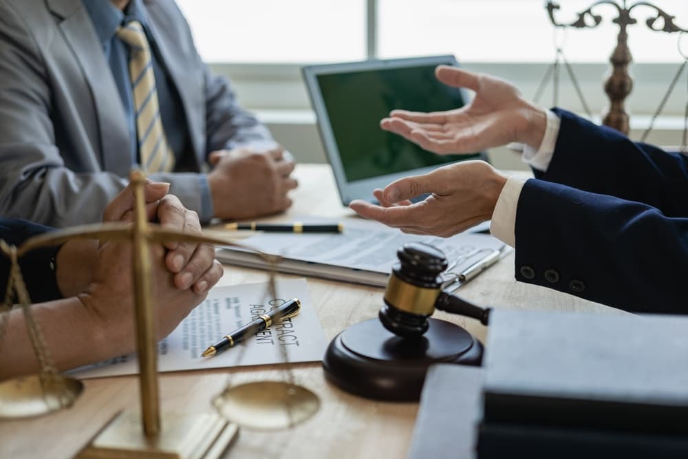 Legal professionals reviewing contract details for accuracy and legality in meeting with hammers and scales on the table.